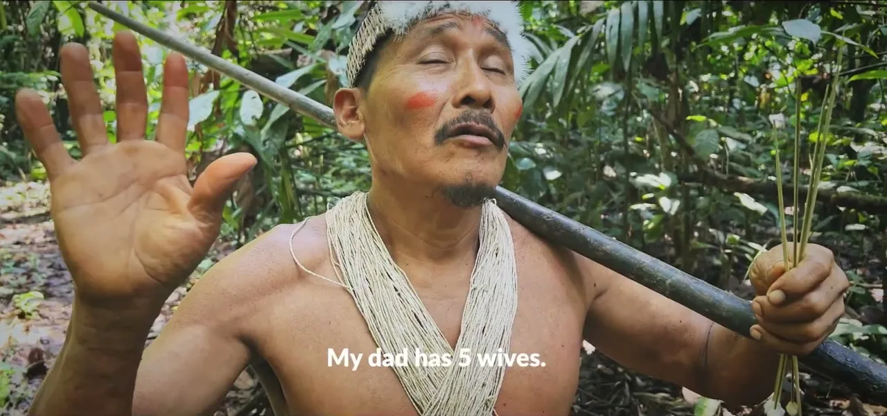 A Waorani man in traditional face paint and feather adornments holding a blowgun in the Ecuadorian Amazon