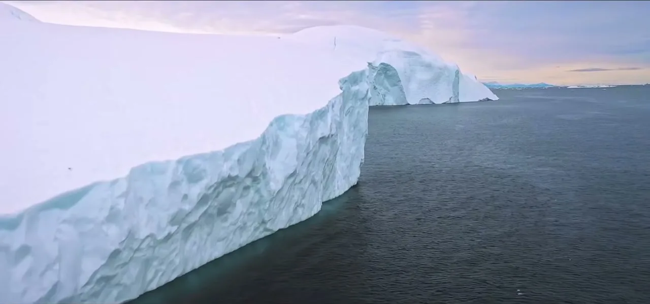 A vast tabular Antarctic iceberg floating on calm water under a golden sky