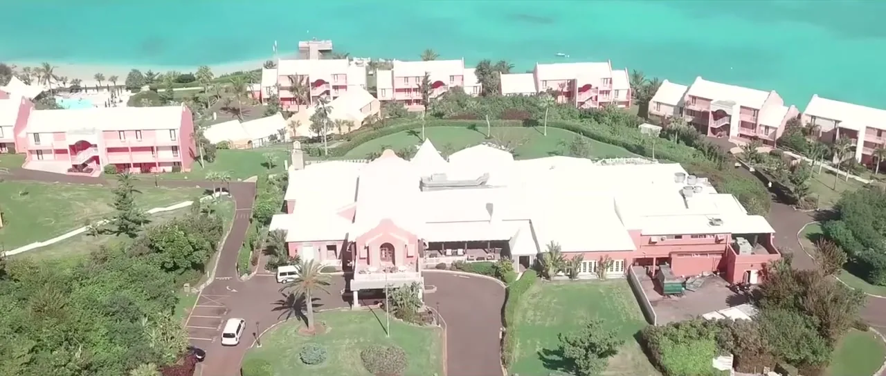 Aerial view of pastel-pink Bermudian cottages beside turquoise water