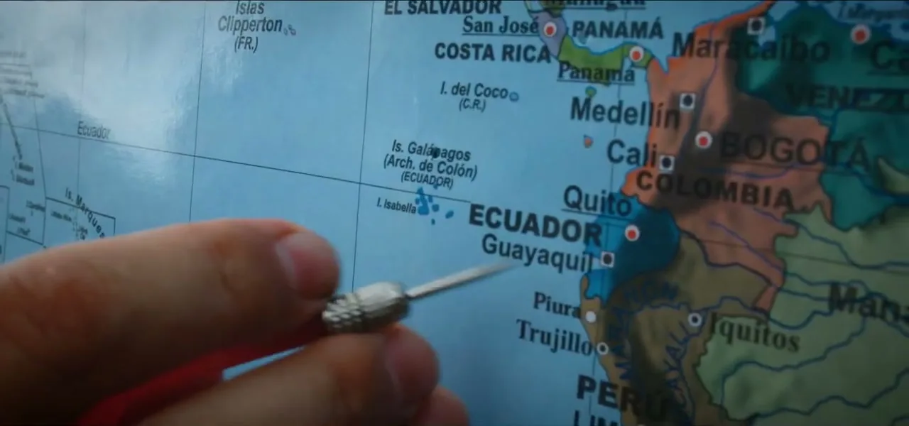 A hand throwing a dart that lands near Ecuador and the Galápagos on a world map