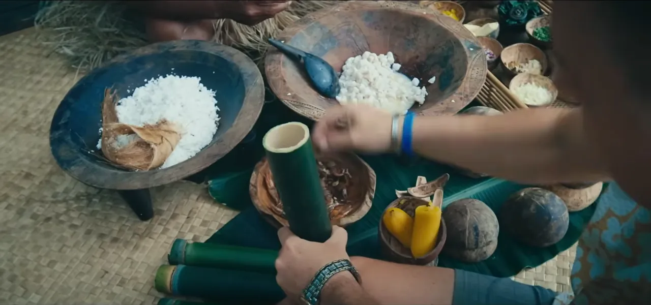 Hands holding a bamboo cooking tube beside bowls of rice and vegetables in Fiji