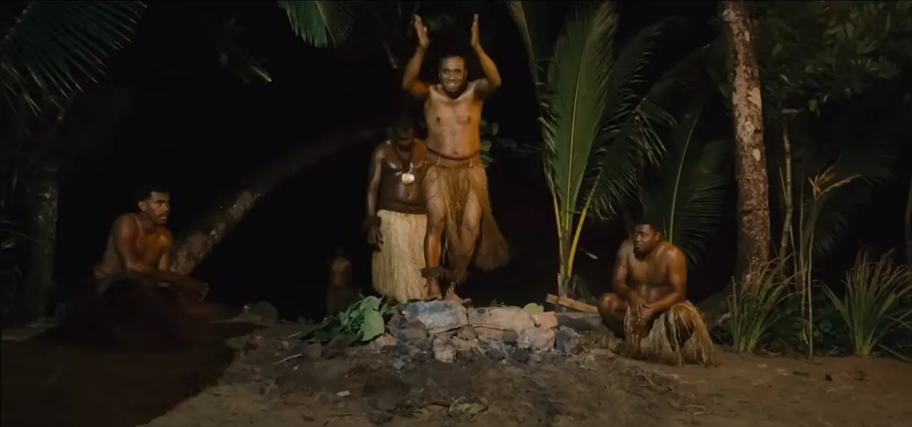 A Fijian firewalker with arms raised over a pit of hot stones at night on Beqa