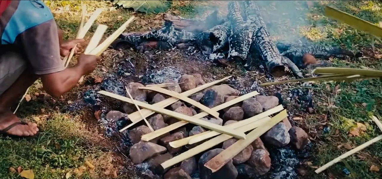 Food wrapped in leaves being placed on hot stones in a Fijian lovo earth oven