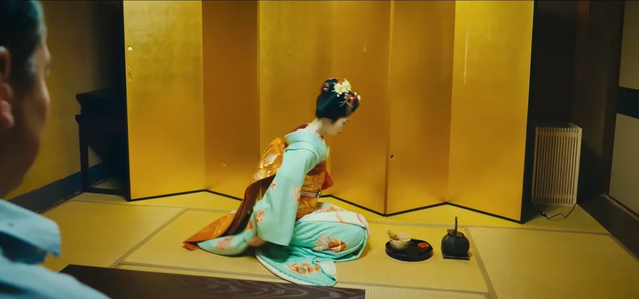A maiko in a light green kimono performing a classical dance in a tatami tea-house room