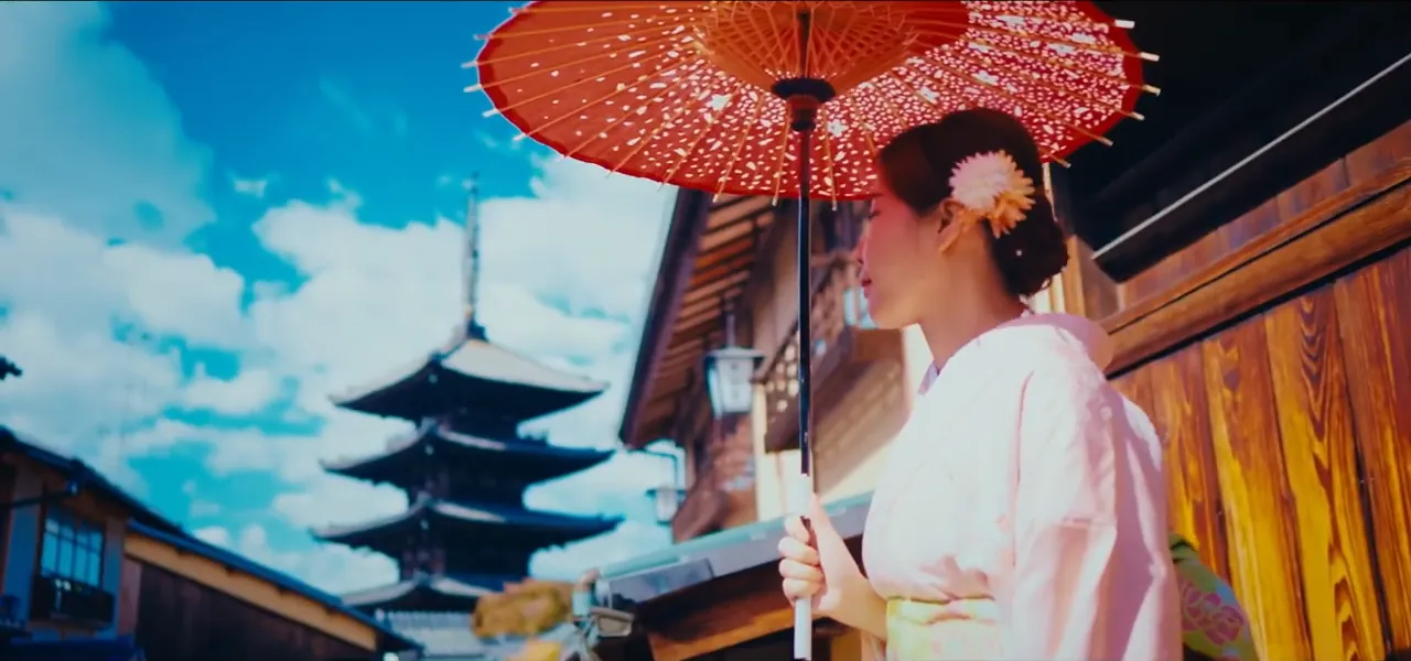 A maiko in a white kimono holding a red parasol beside a pagoda in Kyoto