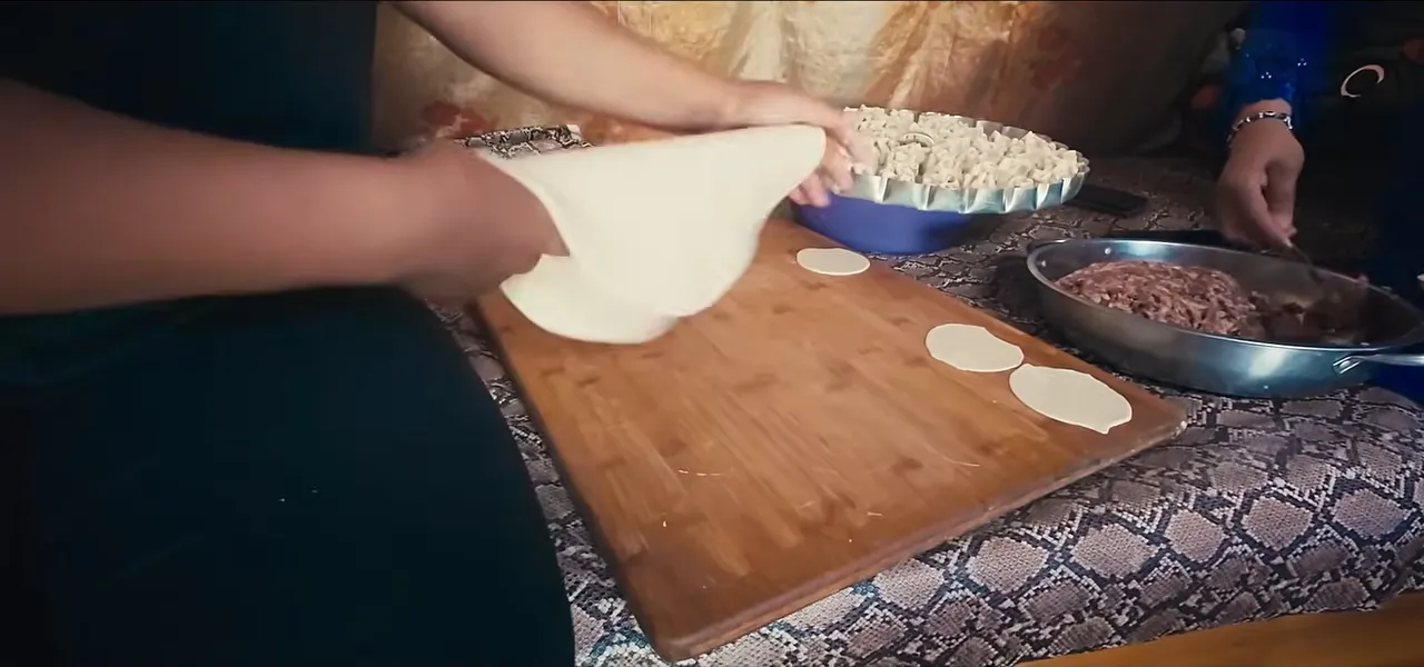 Hands folding buuz, traditional Mongolian steamed dumplings, on a wooden board