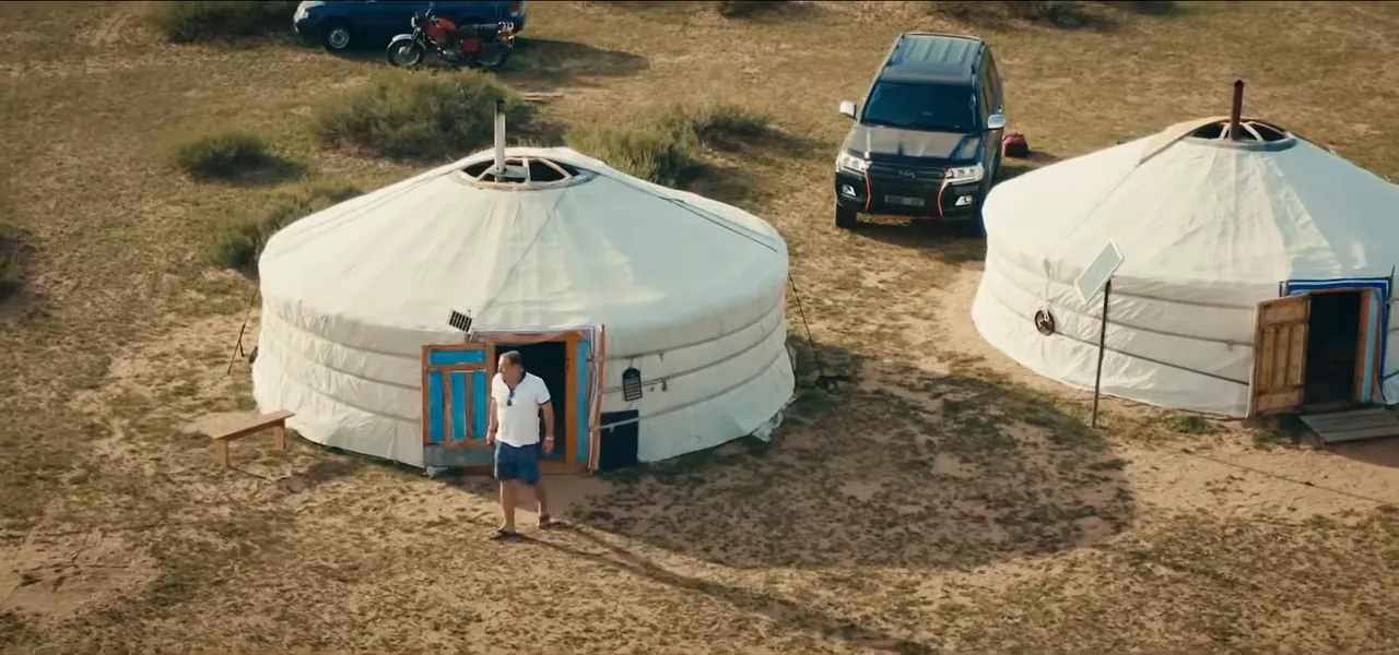 Two white gers and a Land Cruiser on the open steppe, with a person in the doorway