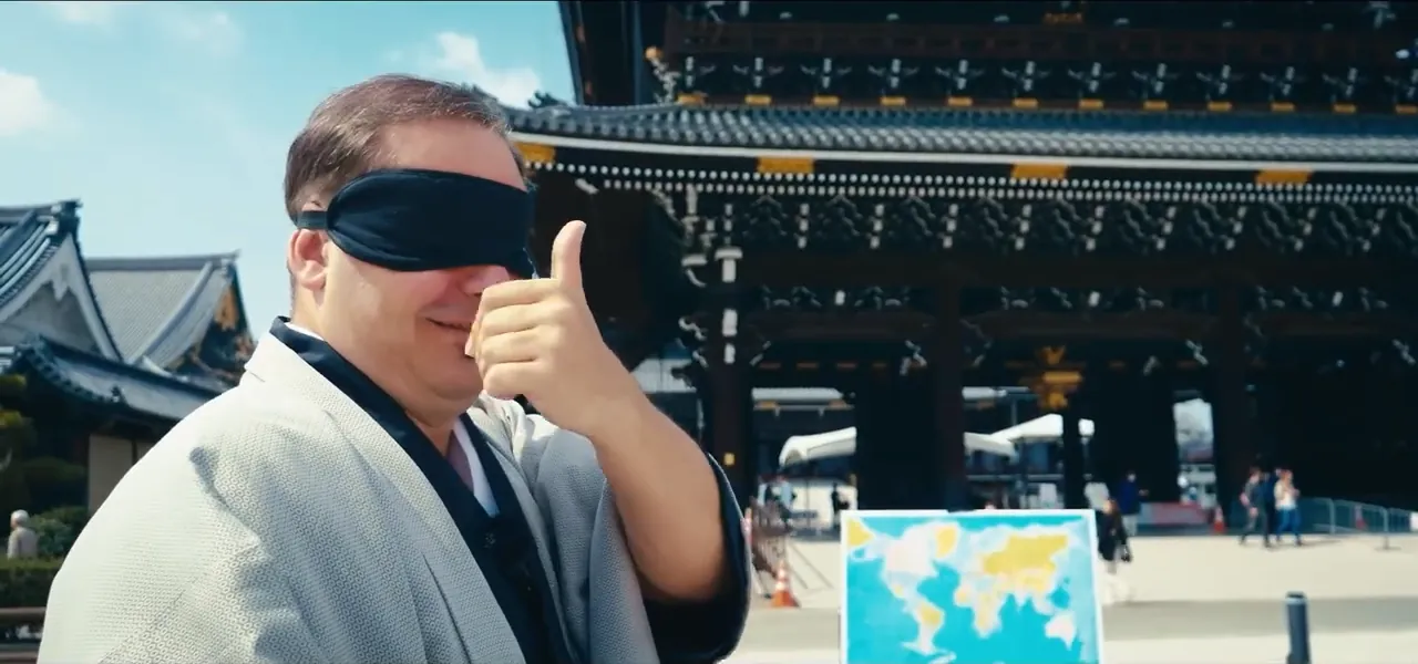 Sorin, blindfolded and in a kimono, throwing a dart at a world map at a temple in Japan