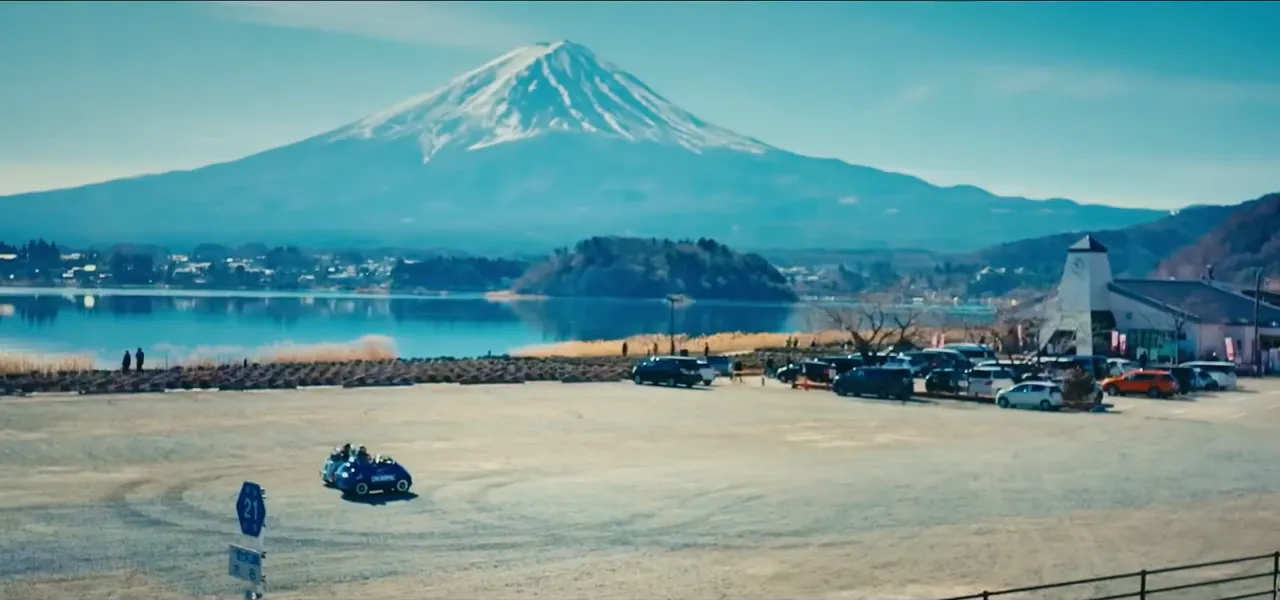 Lake Kawaguchiko with Mount Fuji behind and small vehicles parked at the shore