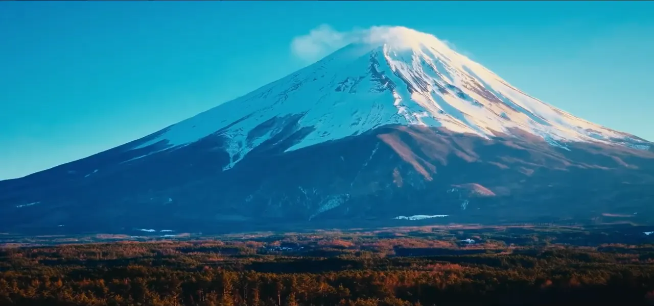 The snow-capped symmetrical cone of Mount Fuji rising above an autumn plain in Japan