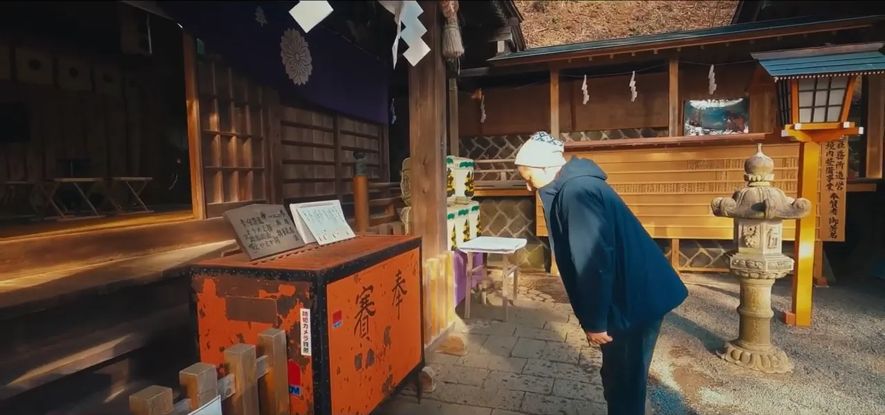 A traditional wooden Sengen shrine dedicated to Mount Fuji, with a visitor at the offering hall