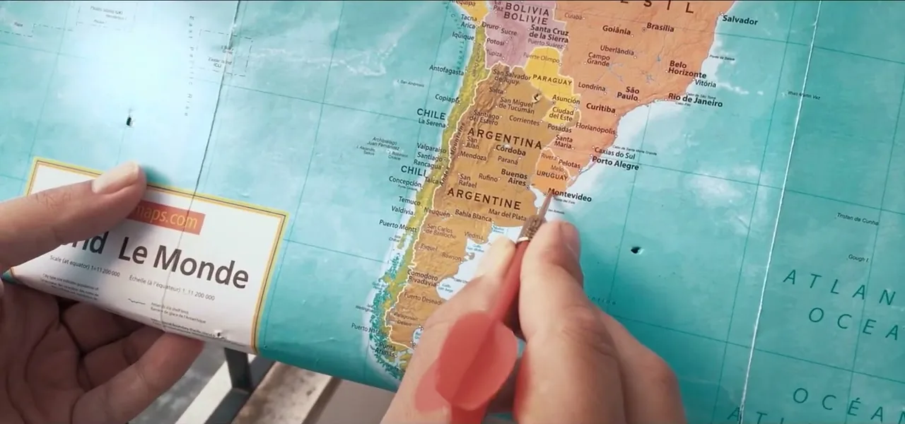 A hand pointing at Uruguay on a world map after the dart throw