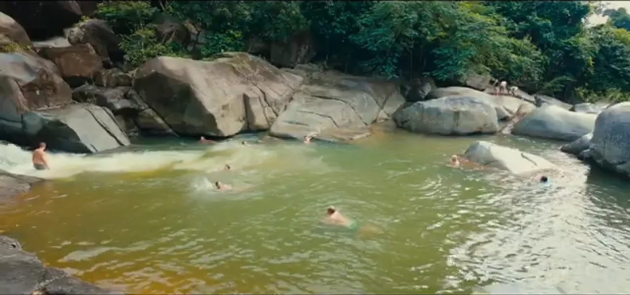 A hidden natural river pool with swimmers among rocks inside El Yunque rainforest, Puerto Rico